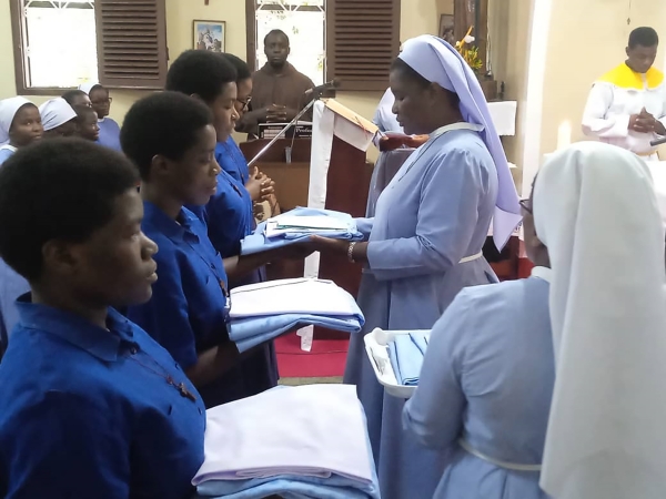 Mhudumu Mkuu wa Shirika la Dada Wadogo, Jimbo Kuu Katoliki la Dar es Salaam, Sista Doreen Mwakaliku, akiwakabidhi nguo baada ya kupandishwa hadhi ya utawa Wapostulanti na kuwa Wanovisi katika Shirika hilo.